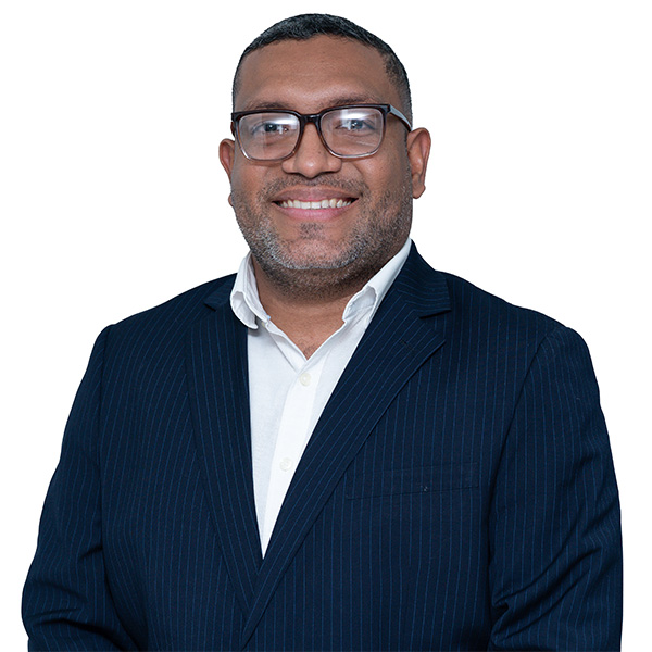 Un hombre con gafas, traje oscuro a rayas y camisa blanca sonríe de pie sobre fondo blanco, transmitiendo confianza y profesionalismo como experto en fisioterapia, hablando sobre ondas de choque para la recuperación de lesiones.