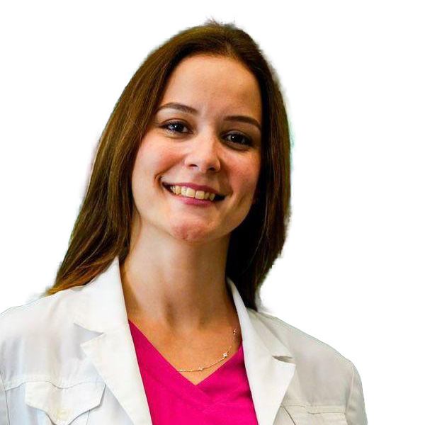 Una mujer de largo cabello castaño sonríe, vestida con una bata blanca de laboratorio sobre un top rosa brillante, de pie sobre un fondo blanco liso, lista para ofrecer fisioterapia y atención experta en ortopedia deportiva.