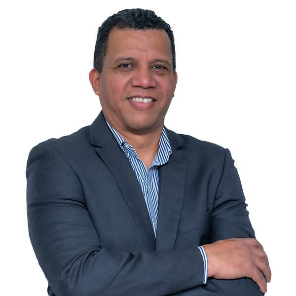 Un hombre con traje oscuro y camisa de rayas, de pie, con los brazos cruzados, sonriendo con confianza, encarna la profesionalidad que se ve en los expertos en fisioterapia, ortopedia deportiva y ondas de choque sobre un fondo blanco liso.